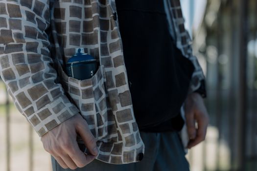 A close-up image showing a spray paint can tucked into a plaid shirt pocket.