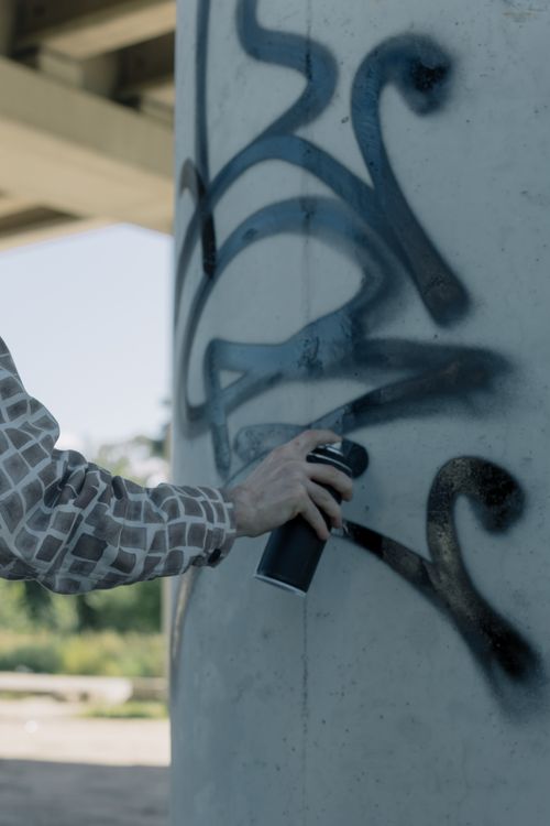 Free Arm holding spray can creating graffiti on outdoor concrete pillar, urban artistic expression. Stock Photo