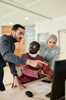 A diverse group of colleagues engaged in a discussion around a computer in a modern office.
