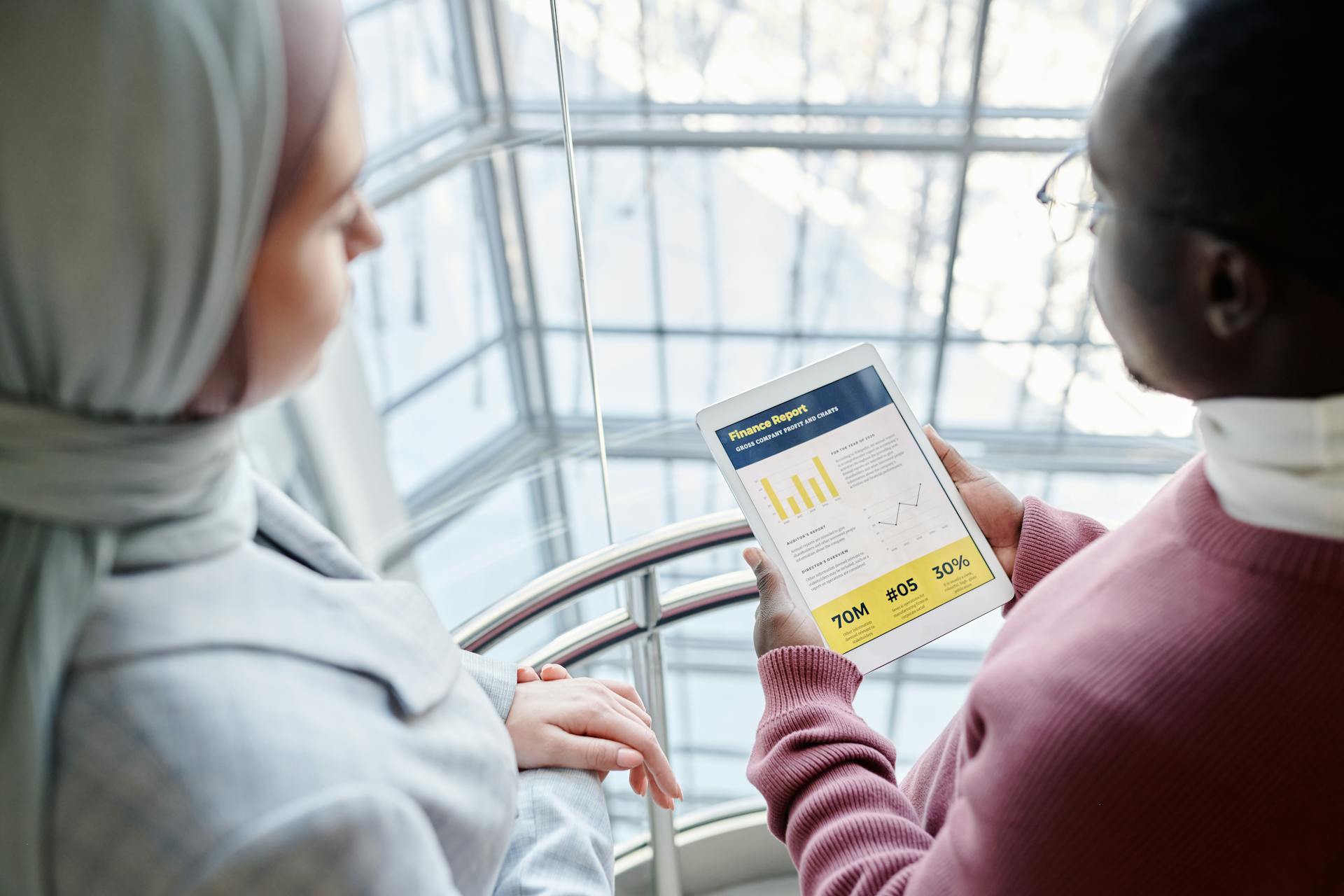 Two business professionals discussing financial data on a tablet in a modern office setting.