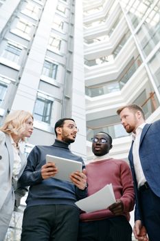 Multiracial professionals engaged in discussion outside a modern office building.