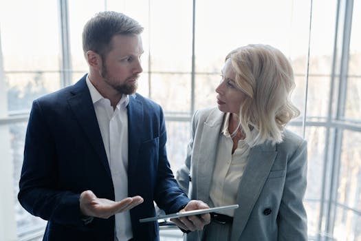 Two business professionals engaged in a discussion with a tablet in a corporate setting.