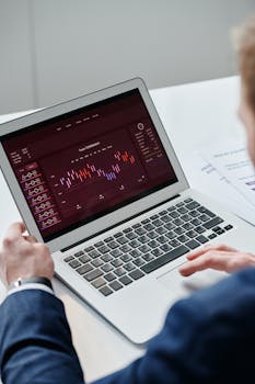 Businessman analyzing trading data on laptop with financial chart on screen, highlighting finance and technology.
