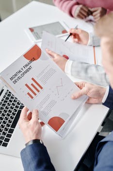 Professional setting with hands analyzing financial documents during a business meeting.