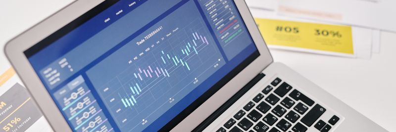 Open laptop displaying financial graphs and analytics with documents nearby, ideal for business presentations.
