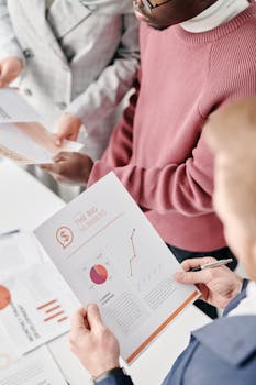 A group of professionals reviewing financial reports with graphs and statistics at a meeting.