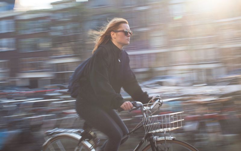 A young woman rides a bicycle quickly through a vibrant urban city
