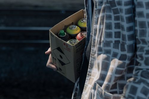 Free Person carrying a box of colorful spray paint cans, suggesting urban art or graffiti. Stock Photo