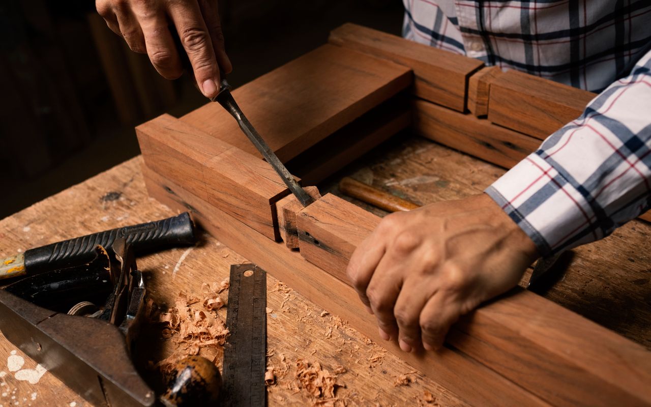 Hands chiselling a joint in hardwood on a workbench with hand plane