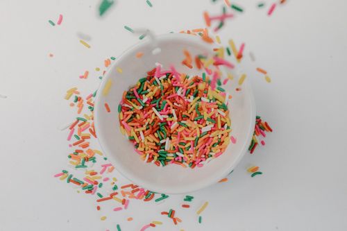Free A top-down view of colorful sprinkles falling into a white bowl. Perfect for dessert themes. Stock Photo