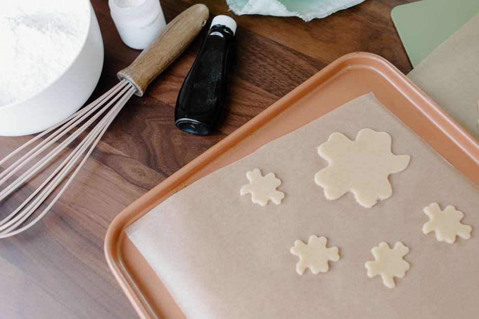 Clover-shaped cookie dough on parchment paper with baking utensils on wooden surface.