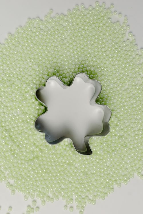 Free Close-up of a shamrock cookie cutter surrounded by green beads, perfect for St. Patrick's Day themes. Stock Photo