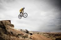 在多云的天空下，一个骑自行车的人大胆地从岩石悬崖上跳了下来