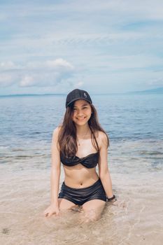 Asian woman smiling in a bikini at the beach, enjoying sunny summer weather.