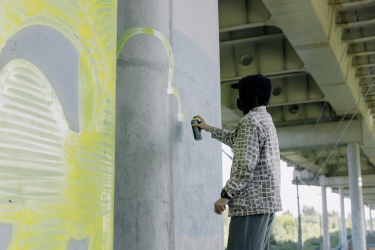 Person Wearing Printed Long Sleeves Spraying Paint On Concrete Wall