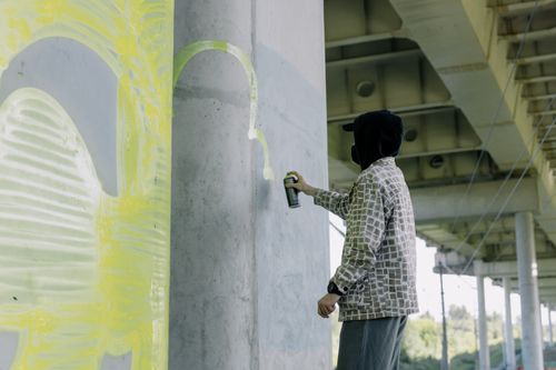 Free Anonymous street artist spray painting graffiti on an urban concrete wall under a bridge. Stock Photo