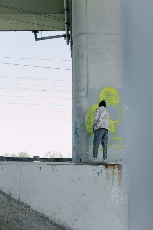 Person in Hoodie Jacket Doing Graffiti on a Wall