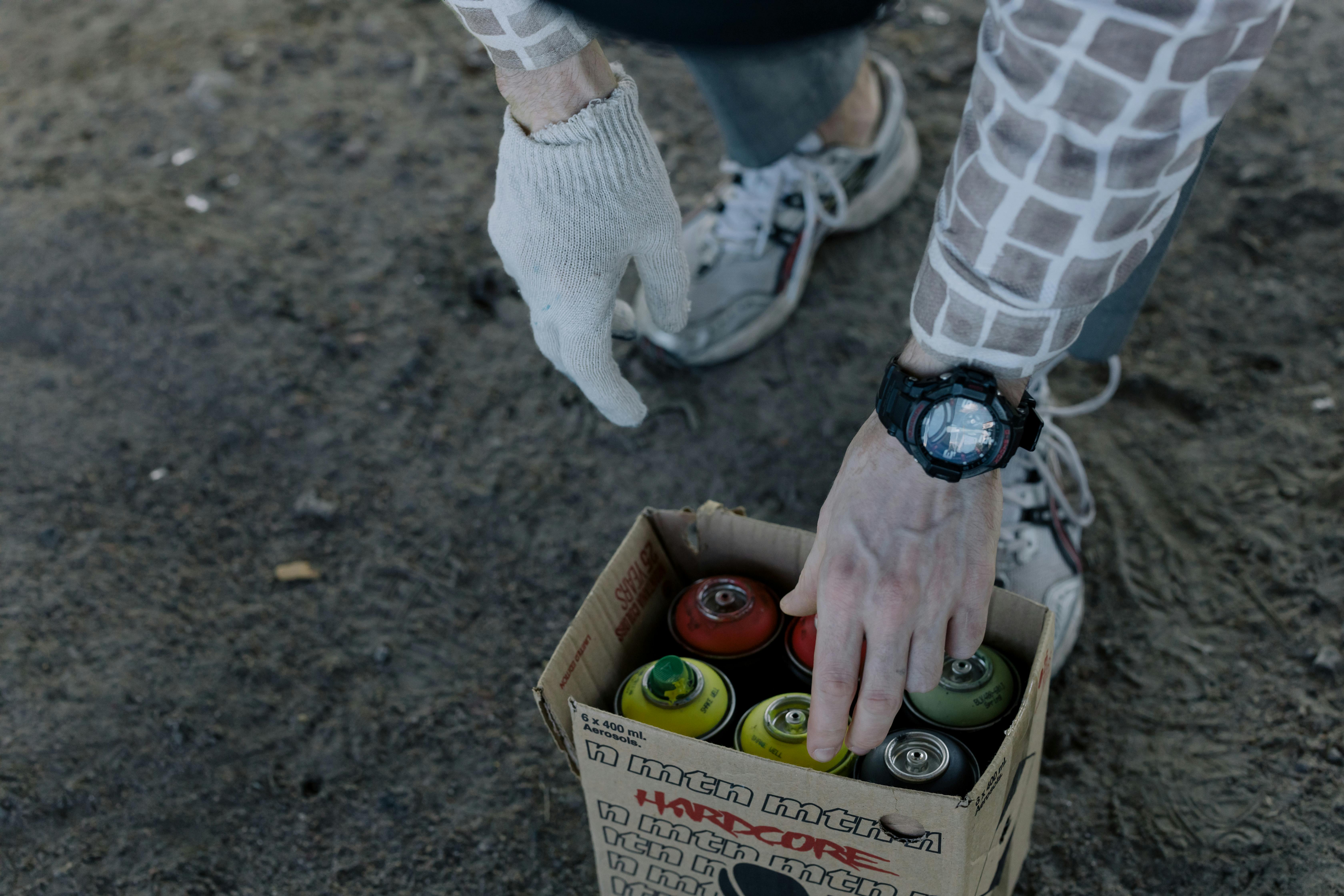 Close-up of hands picking spray paint cans from a box, ideal for street art concepts.