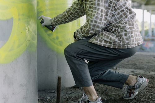 Free A street artist in plaid shirt spray-painting graffiti on a concrete wall under a bridge. Stock Photo