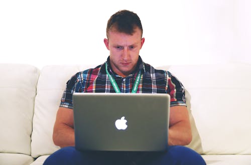 Man Using Macbook While Sitting on White Sofa