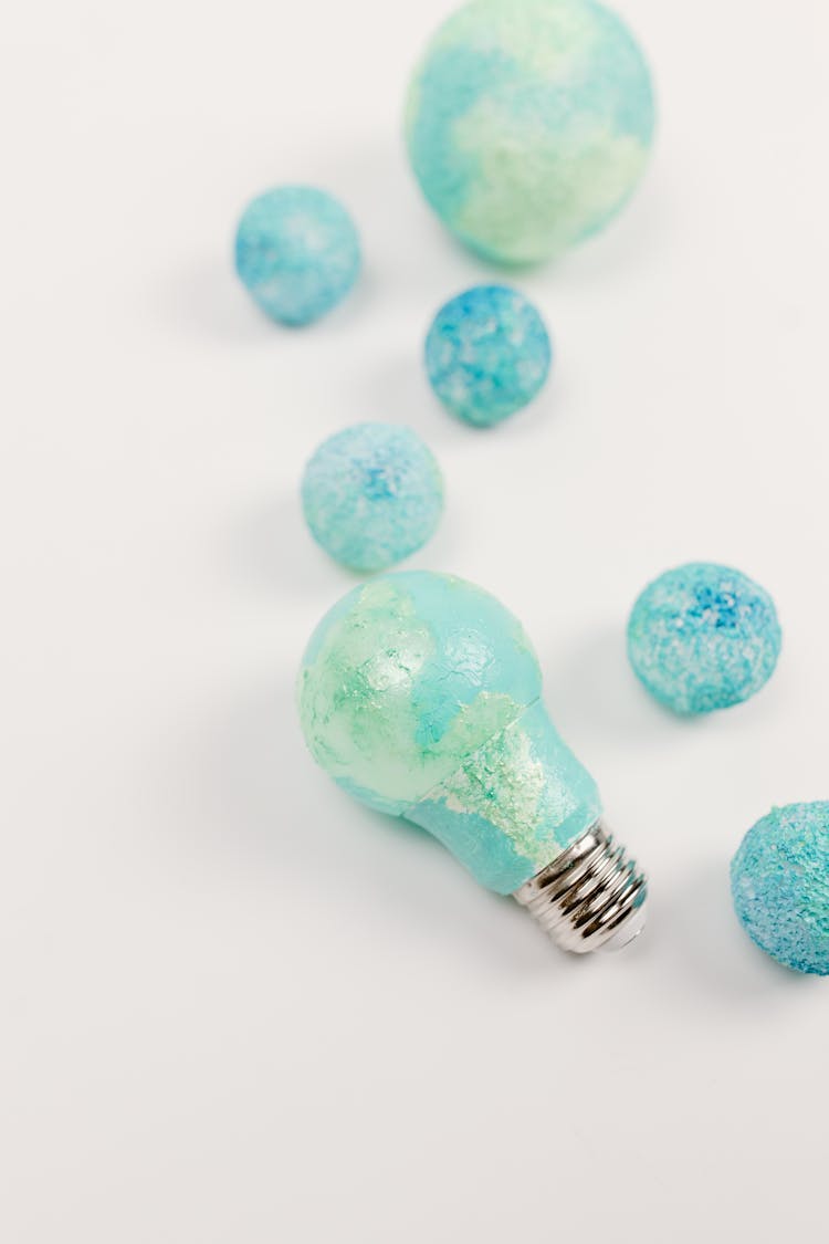 Light Bulb And Balls Painted In Blue And Teal Color On White Surface