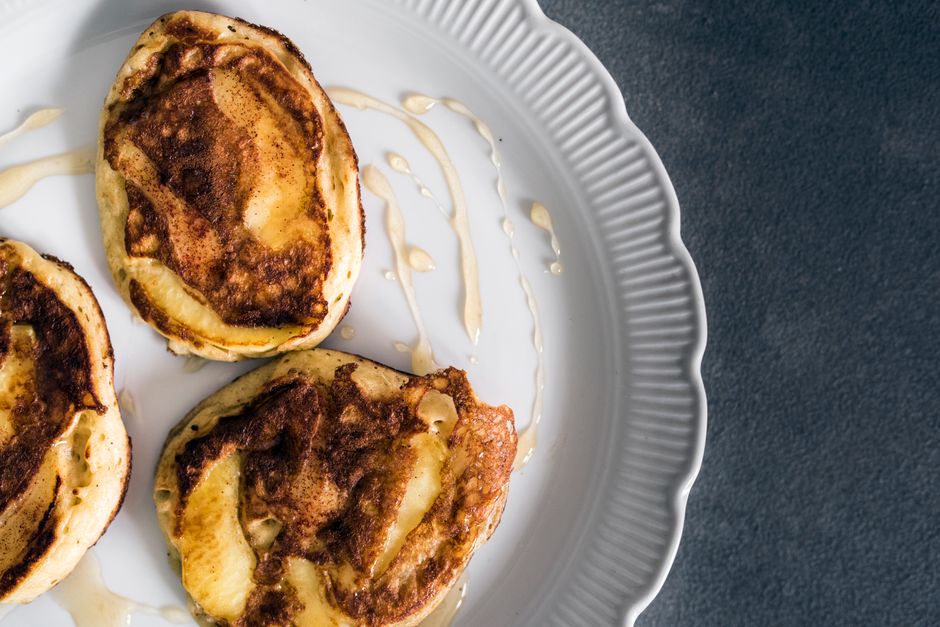 Top view of freshly baked cinnamon apple pancakes drizzled with syrup on a white plate.