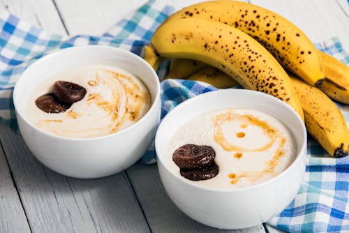 Bananas Beside Two White Bowls with Heavy Cream