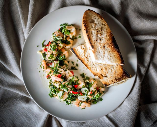 Top view of shrimp with herbs and toasted bread on a white plate.