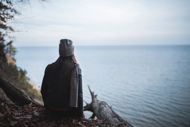 Woman Sitting On The Edge Of A Cliff Looking At The Sea