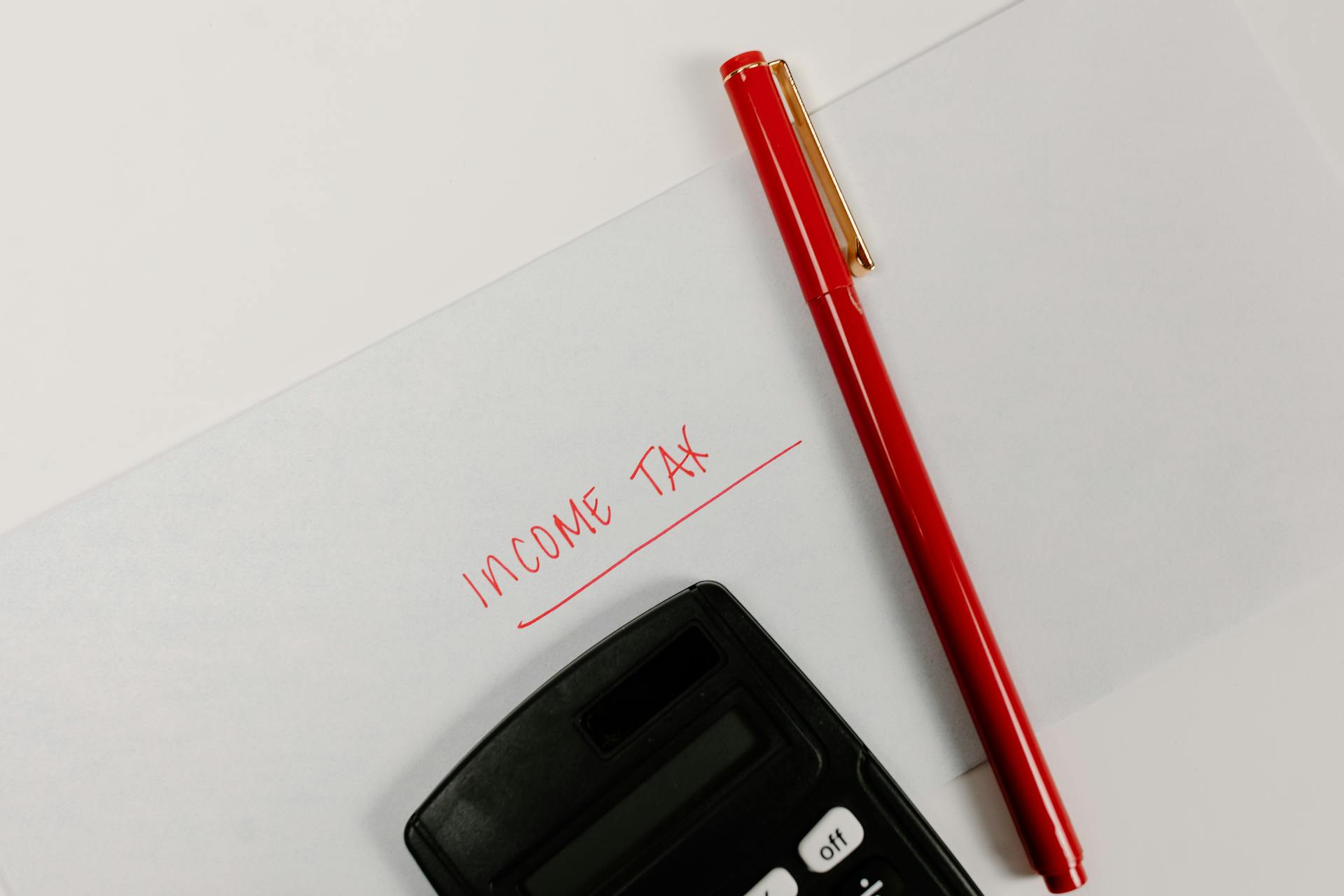 Close-up of a calculator and red pen on paper labeled 'Income Tax', representing financial planning.