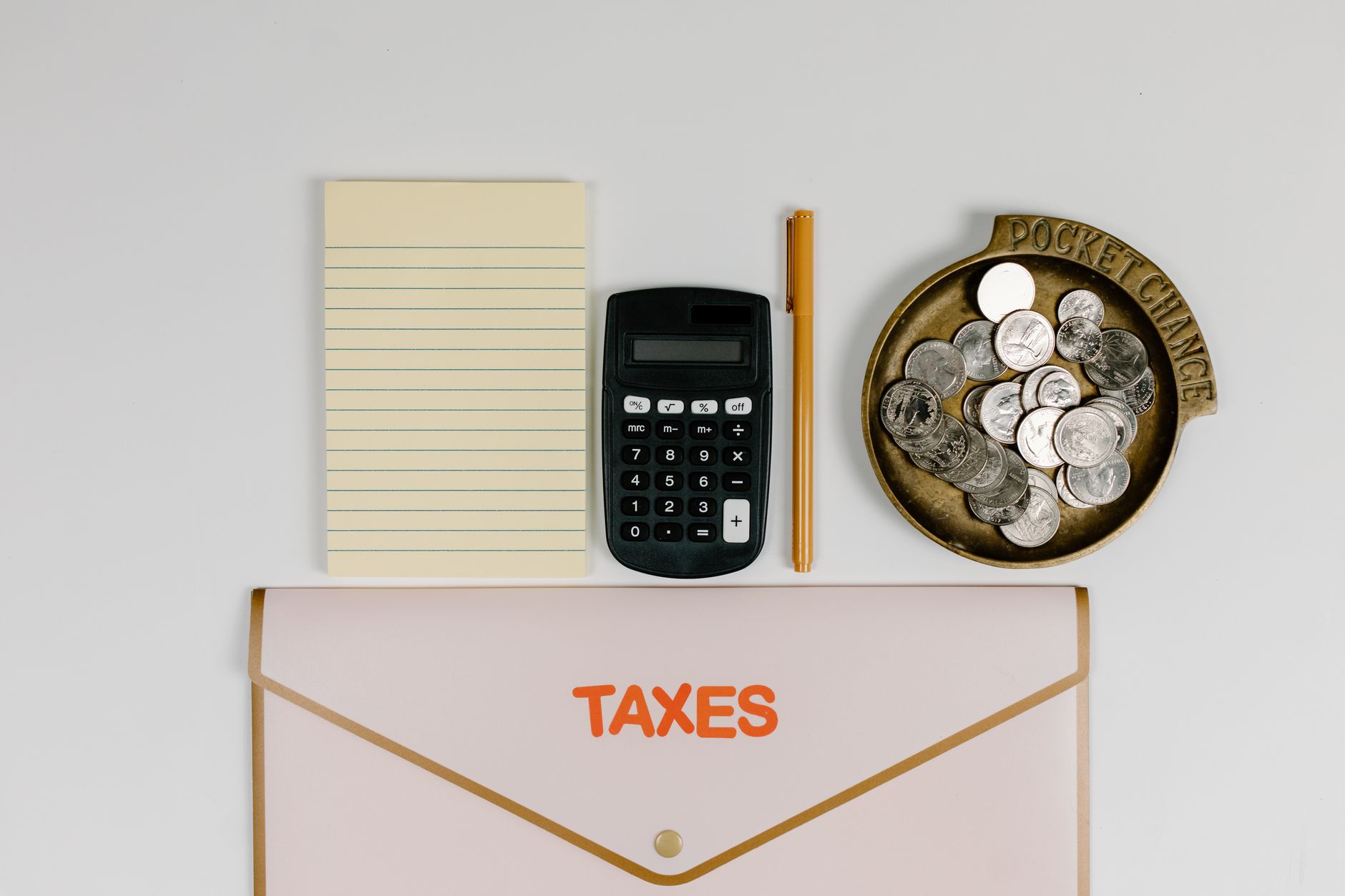 A flat lay of tax preparation essentials: calculator, coins, notepad, pen, and folder.