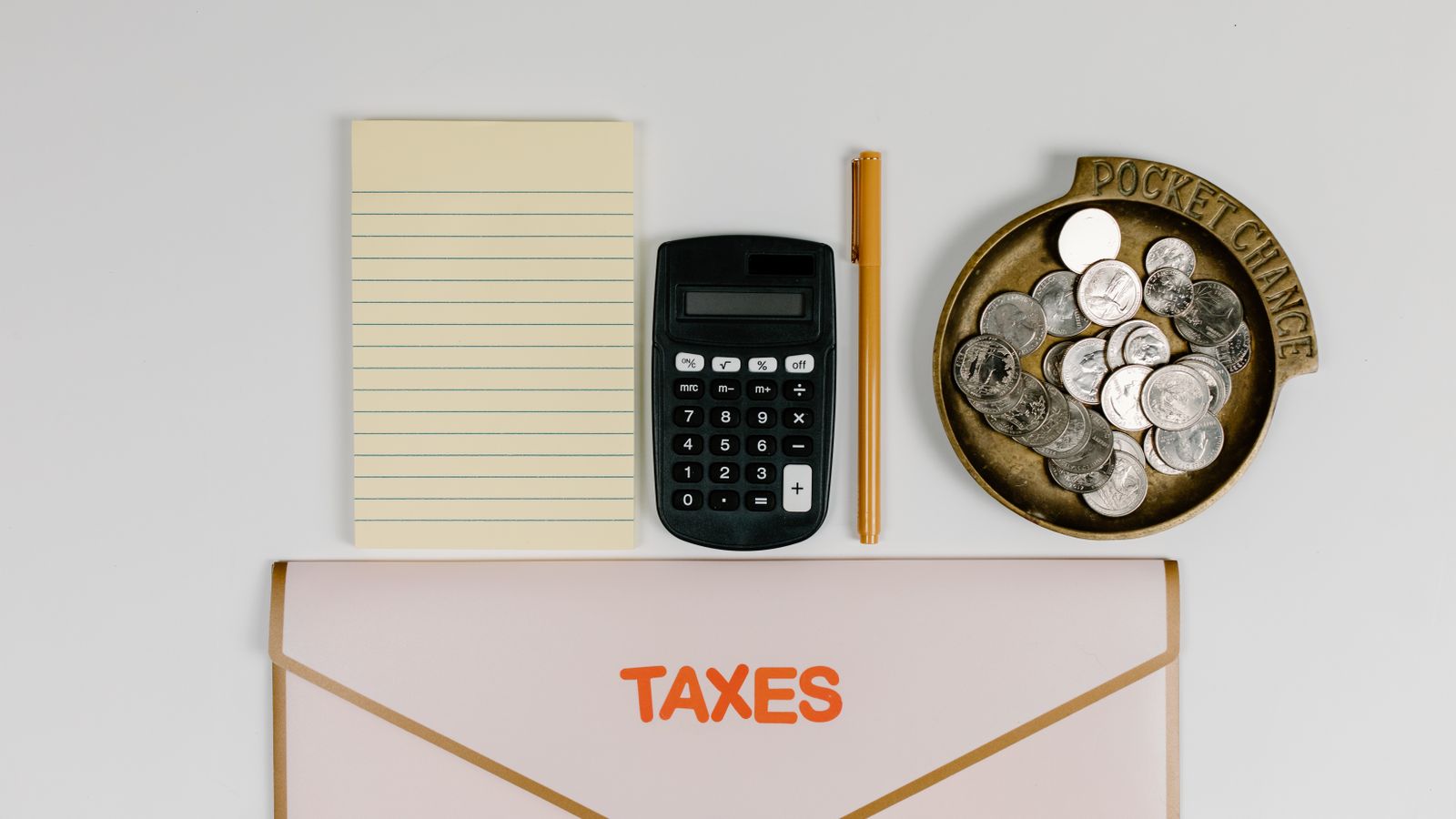 A flat lay of tax preparation essentials: calculator, coins, notepad, pen, and folder.