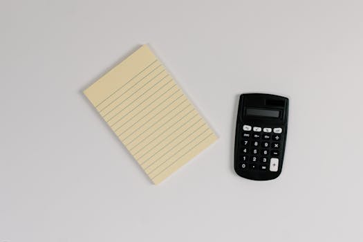 Top view of a minimalist setup with a yellow lined notepad and a black calculator on a white surface.