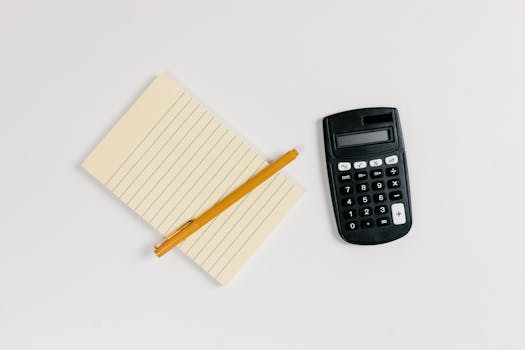 Minimalist flat lay of a calculator and lined notepad with a gold pen on a white surface.