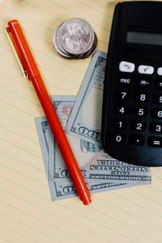 Close-up of a pen, calculator, and cash on a notepad, representing financial planning.