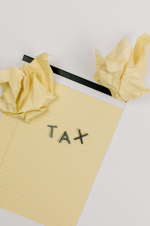 Free Yellow notepad featuring the word 'TAX' with crumpled paper, symbolizing taxation and paperwork frustration. Stock Photo