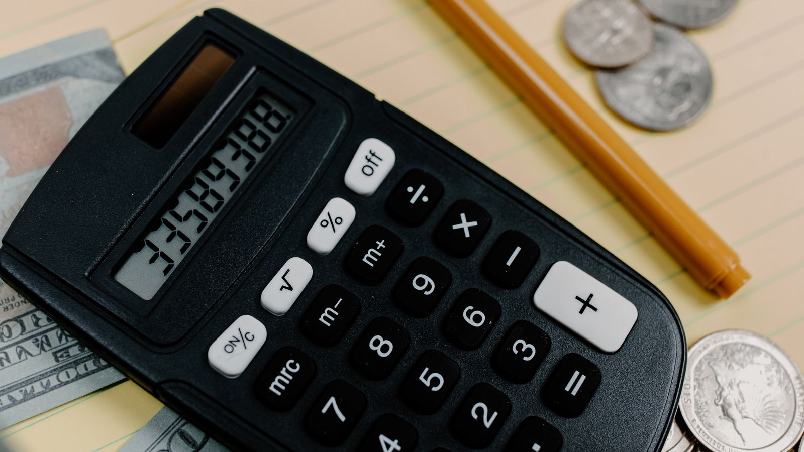 A calculator, cash, coins, notepad and pen arranged on a desk