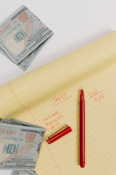 Close-up of a red pen and tax notes on yellow paper with US dollar bills.