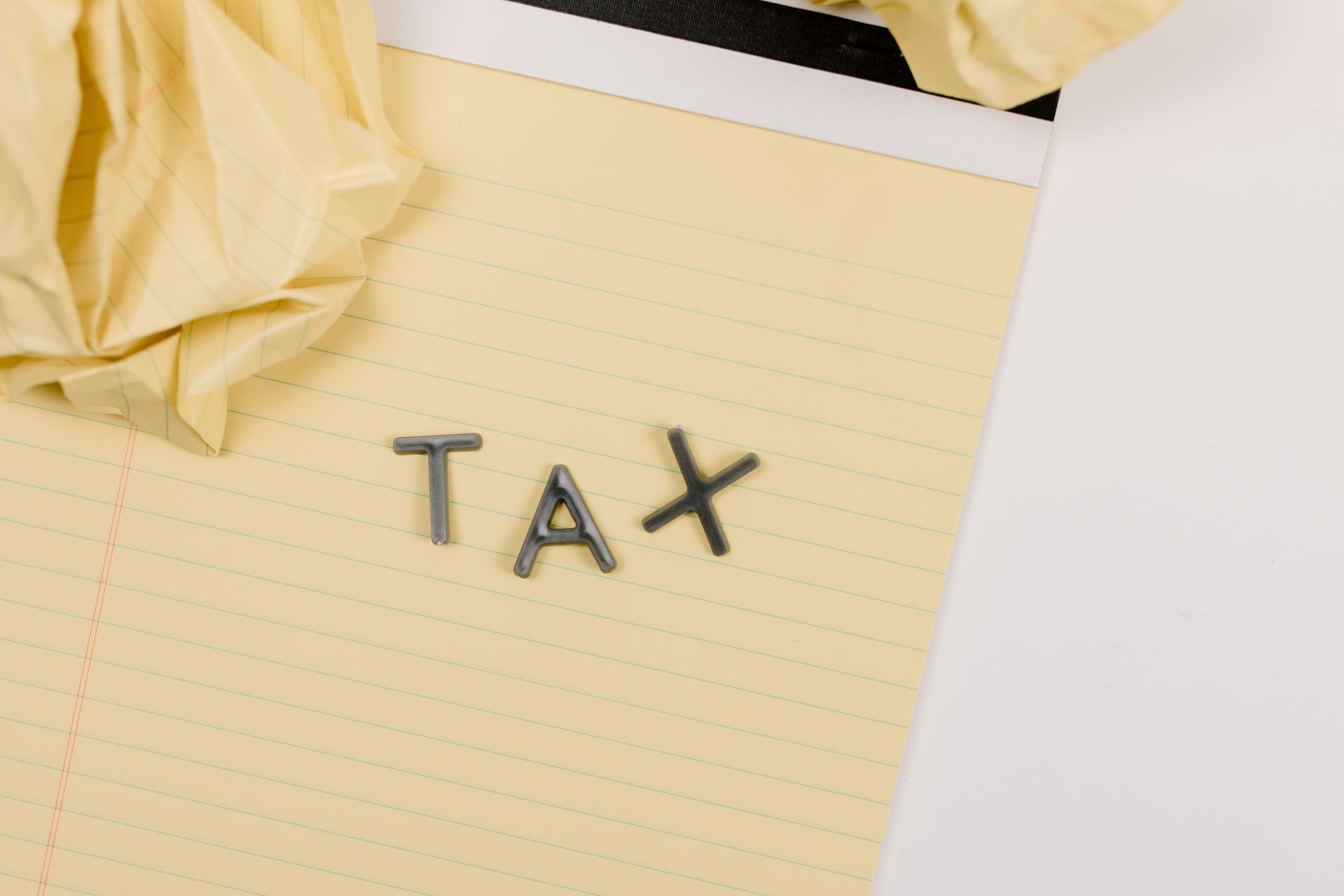 Close-up of a yellow lined paper with metal letters spelling 'tax', surrounded by crumpled paper.