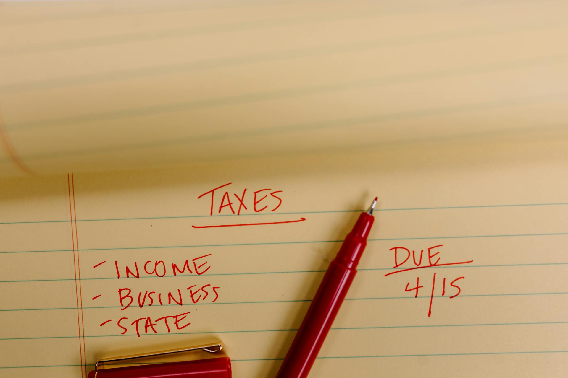 Close-up of tax-related notes on a yellow legal pad with red pen, highlighting important due dates.