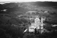 Aerial view of a historic church surrounded by Tuscan countryside, captured in monochrome.