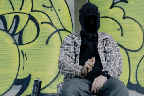 Free Hooded street artist sitting in front of vibrant graffiti wall with spray can nearby. Stock Photo