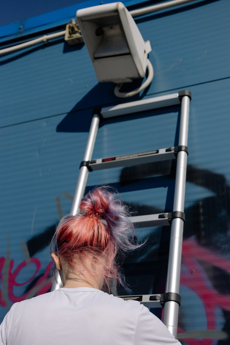A Woman In White Shirt Climbing A Ladder