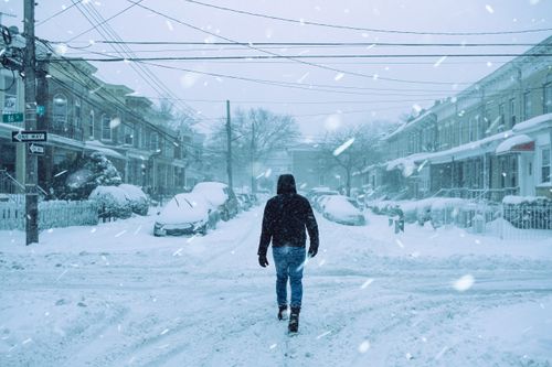 Free Full body back view of faceless man in outerwear strolling on crossroad on snowy street with parked cars and residential buildings during snowfall Stock Photo