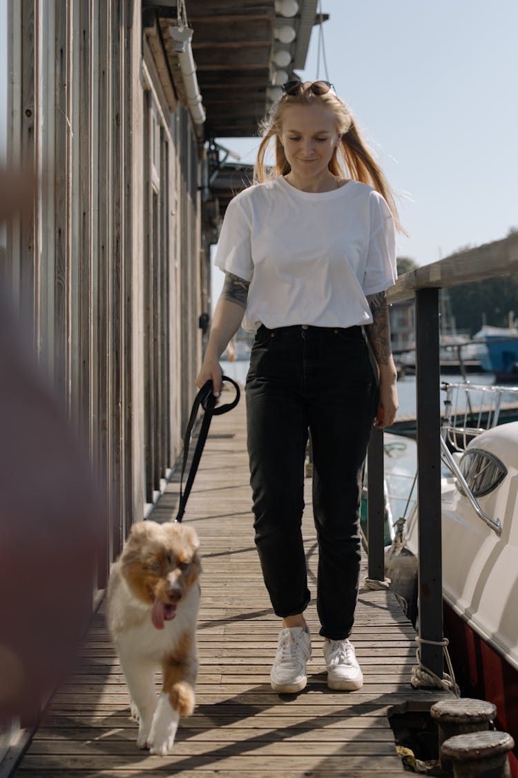 Woman In White Shirt Holding The Leash Of A Dog