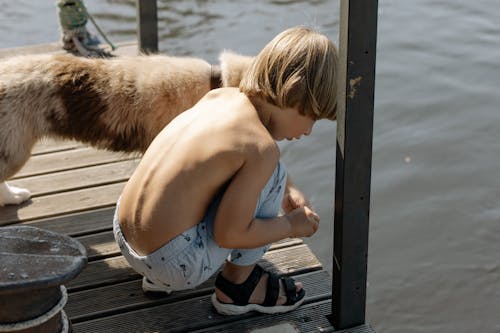 Photo of a Shirtless Boy Crouching Beside a Dog