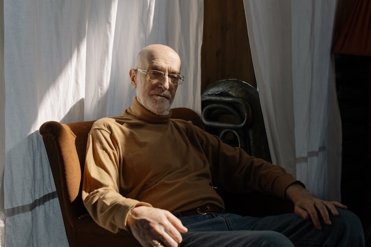 An Elderly Man In Brown Long Sleeves Sitting On The Chair