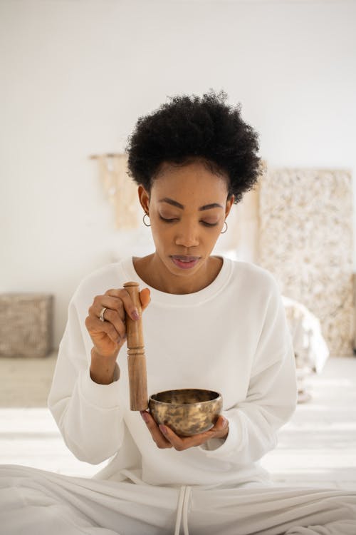 A Woman in White Long Sleeves Using a Singing Bowl