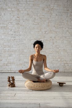 Peaceful woman meditating on a cushion in a bright, minimalist room.