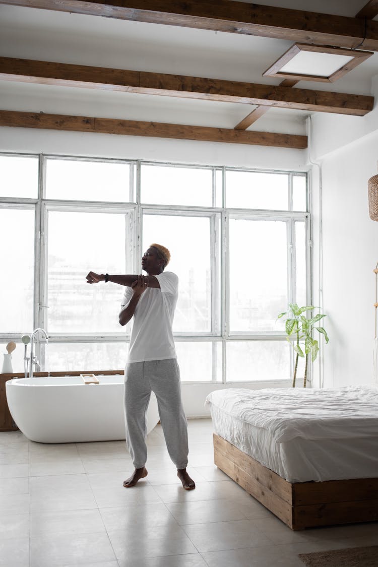 Man In White Shirt Stretching Arms Near A Bed